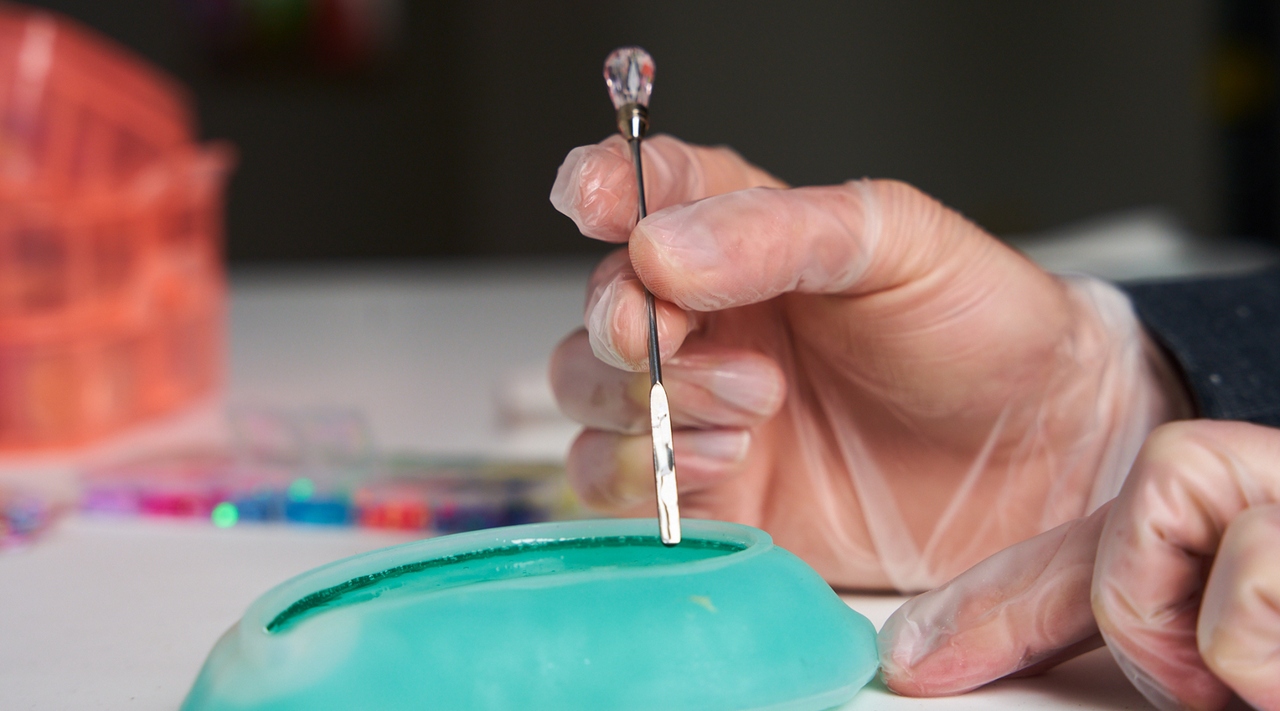 hands with gloves dipping a small tool into a silicone mold full of blue tinted resin