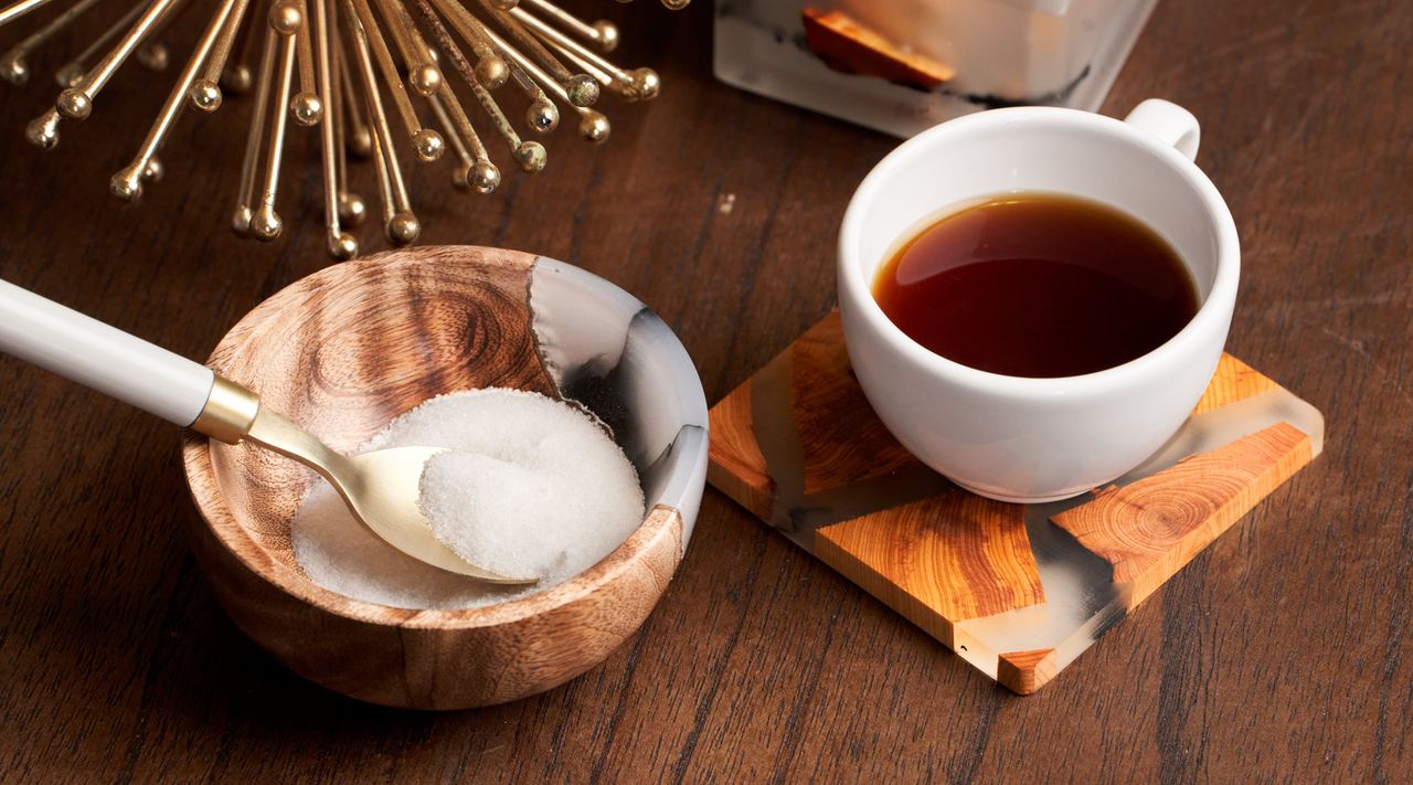 a live edge resin coasters with a hot coffee mug sitting on top of it showcasing epoxy is heat resistant, with an epoxy bowl next to it sitting on a coffee table