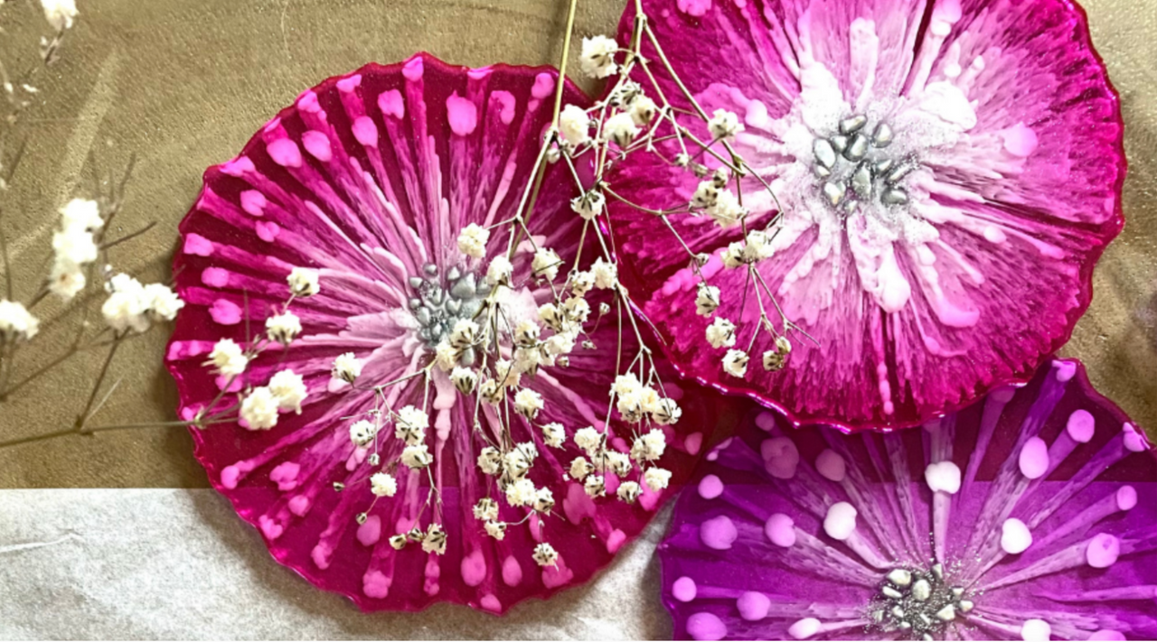 three pink and purple 3d floral resin coasters sitting on top of a wooden surface with a linen cloth