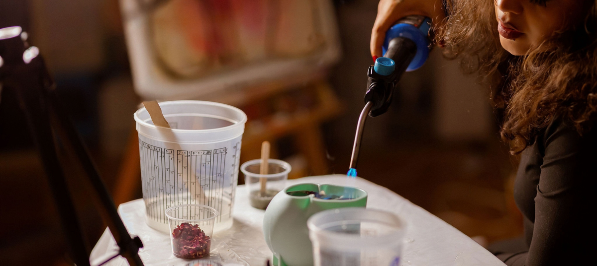 Woman using a handheld torch to remove air bubbles from a glossy epoxy resin project in her art studio.