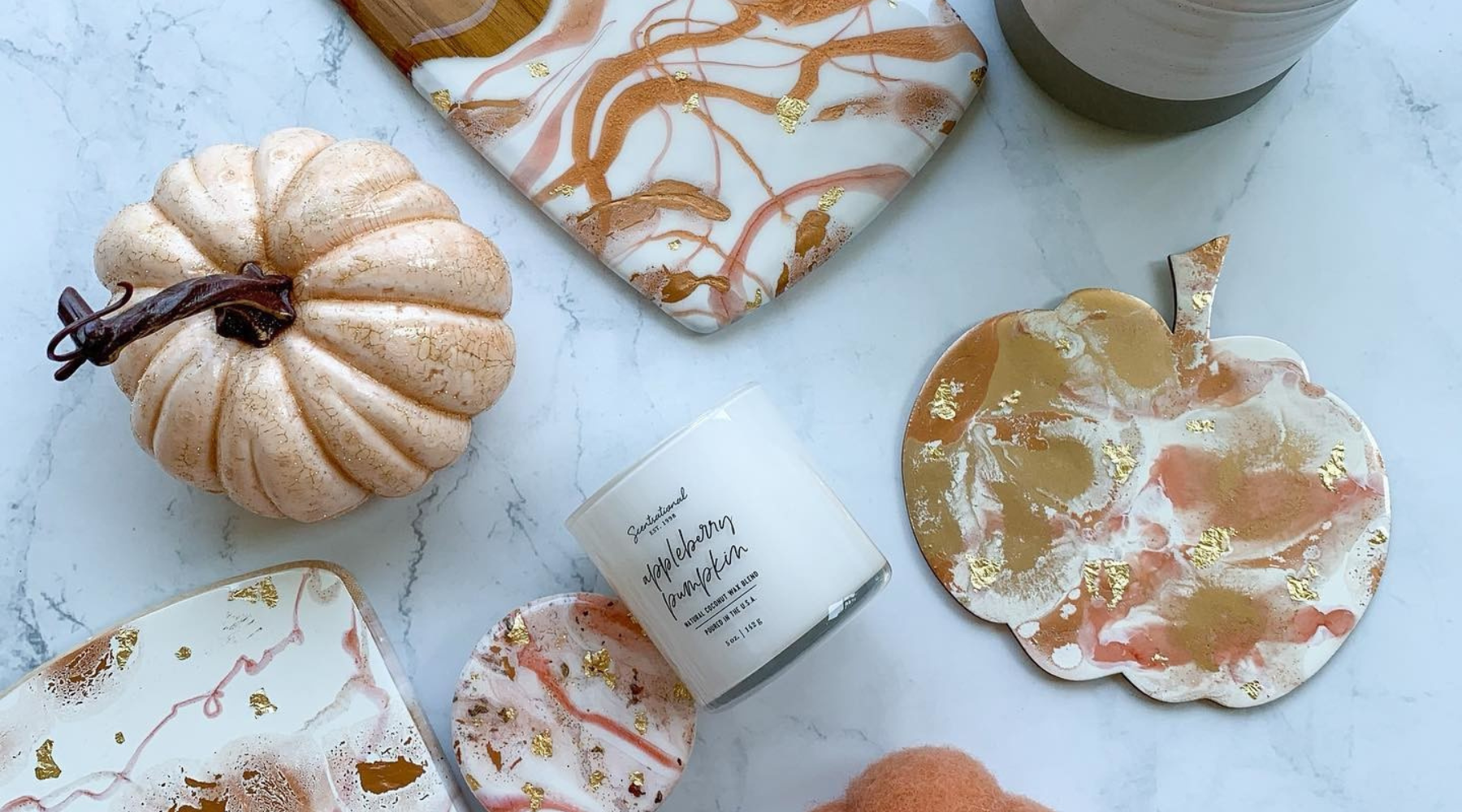Assorted DIY Halloween home decor and crafts with marbled coasters, a pumpkin, and a maple-bourbon scented candle