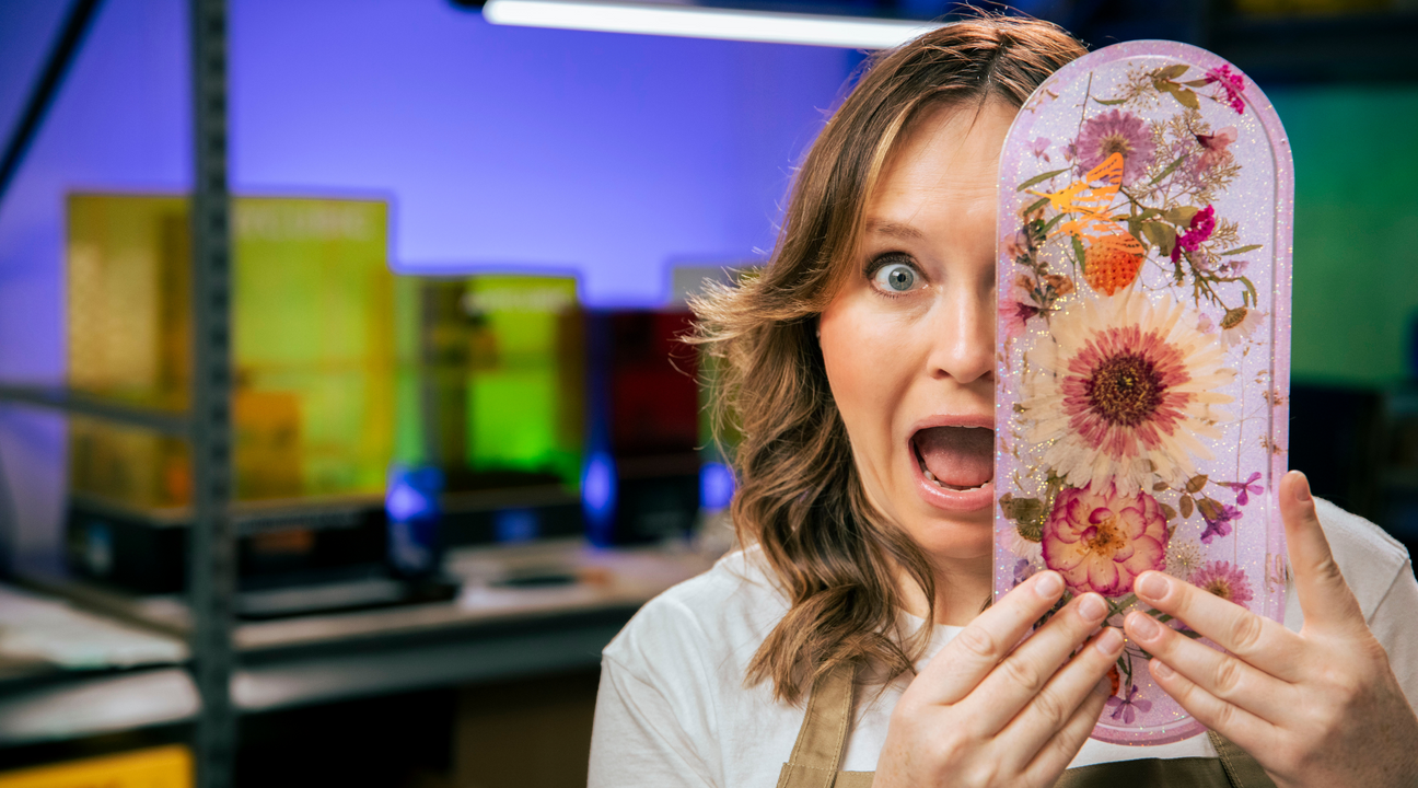 woman standing with an epoxy resin floral trinket tray in pink covering half of her face in a workshop
