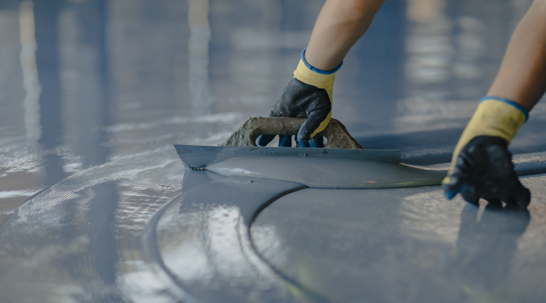 A person wearing protective gloves smooths out a freshly applied layer of epoxy resin on a large surface with a metallic squeegee tool, reflecting a meticulous and professional application process