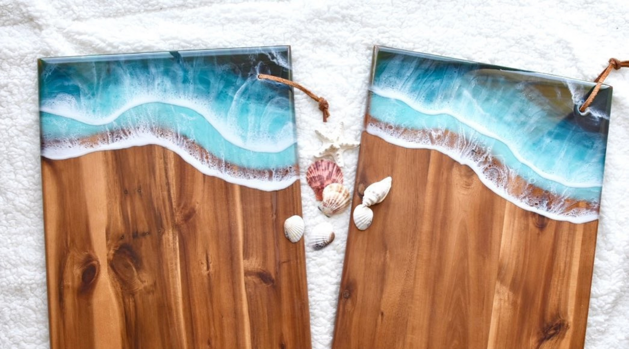Epoxy resin ocean art on wooden boards, depicting turquoise waves with white foam, accented with scattered seashells on a fluffy white background.