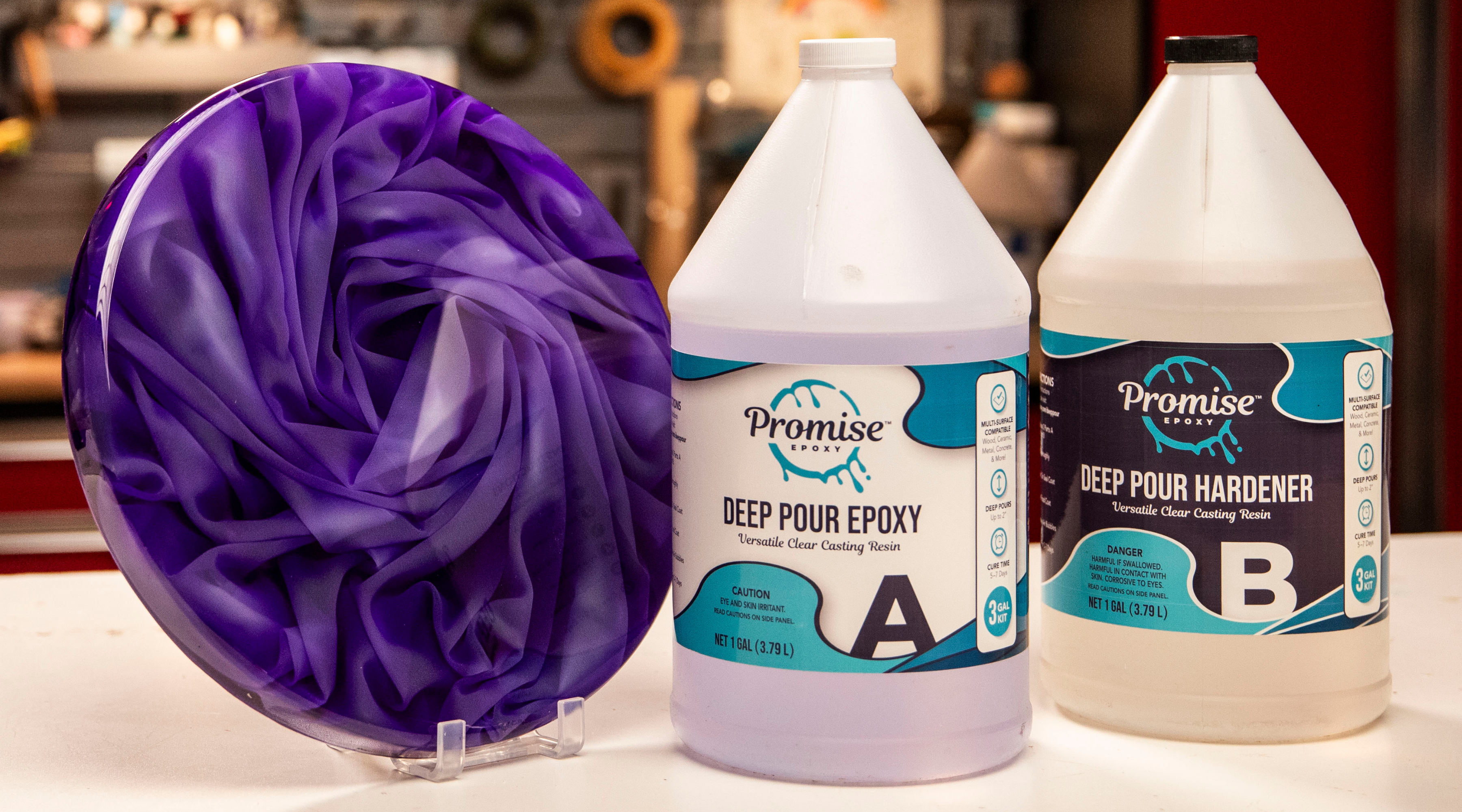 chiffon fabric encapsulation in deep pour epoxy with a purple tint round propped up on a white table next to two bottles of Promise Deep Pour Epoxy