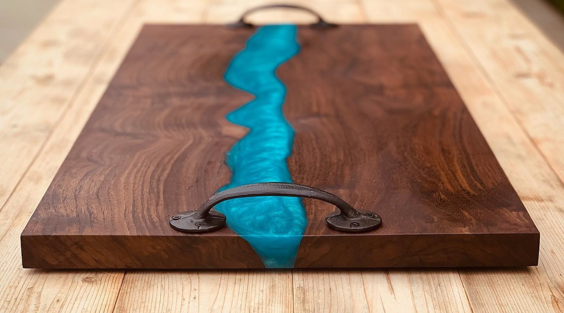 A walnut charcuterie board with an epoxy river pour down the middle in bright blue sitting on a light wooden surface ready for cleaning an epoxy surface